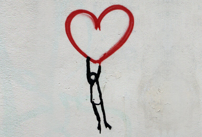 Foto von einem Wandgrafitti: Eine Figur, die an einem roten Herz hängt.