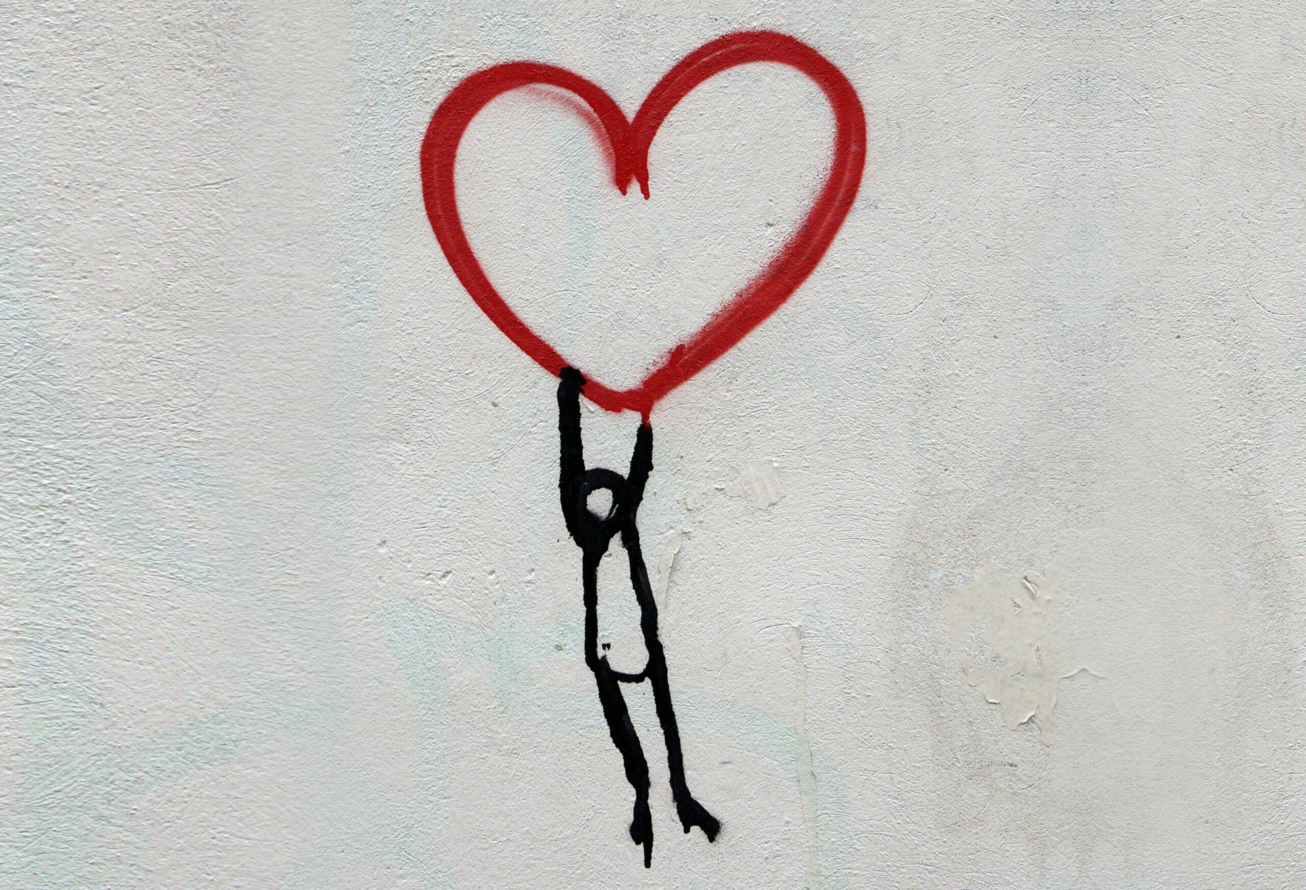 Beitragsbild zu Verschwörungserzählungen: Wandgrafitti: Figur, die rotes Herz hochhält.