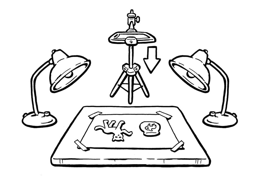 Legefilm Illustration in schwarz-weiß: Auf einem Tisch liegen zwei Bilder, neben dem Tisch stehen rechts und links Lampen, vor dem Tisch steht eine Kamera auf einem Stativ. Die Kamera filmt die zwei Motive auf dem Tisch von oben.